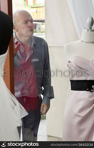 Senior man looking at wedding dress displayed on window in bridal store