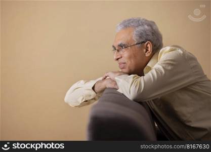Senior man looking away while leaning on sofa 