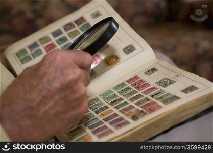 Senior man looks at stamp collection with magnifying glass