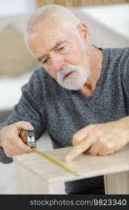 senior man marking a measurement on a wooden plank