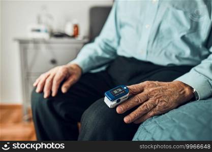 Senior man measuring the degree of oxygen saturation of the blood and heart rate at home using pulse oximeter. Home treatment of virus. Checking health condition. Coronavirus pandemic. Covid-19 outbreak