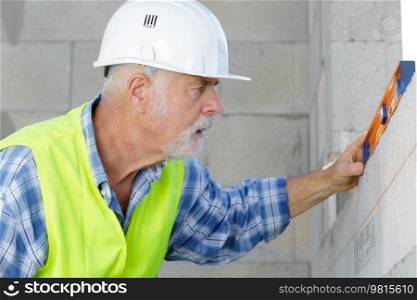 senior man measuring wall with construction level