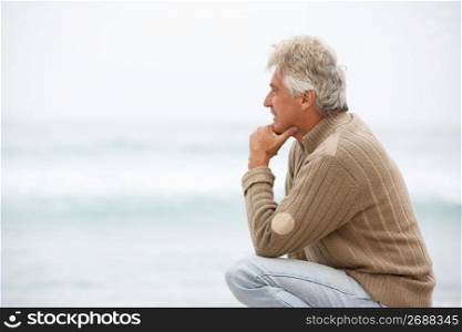 Senior Man On Holiday Kneeling On Winter Beach