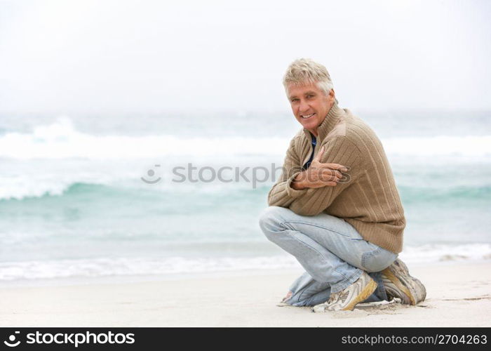 Senior Man On Holiday Kneeling On Winter Beach