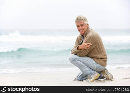 Senior Man On Holiday Kneeling On Winter Beach