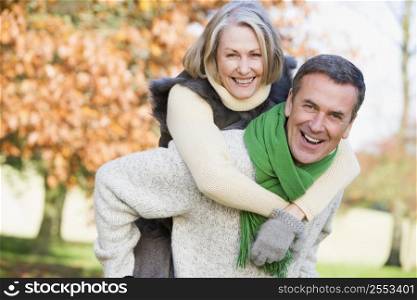 Senior man outdoors piggybacking woman and smiling (selective focus)