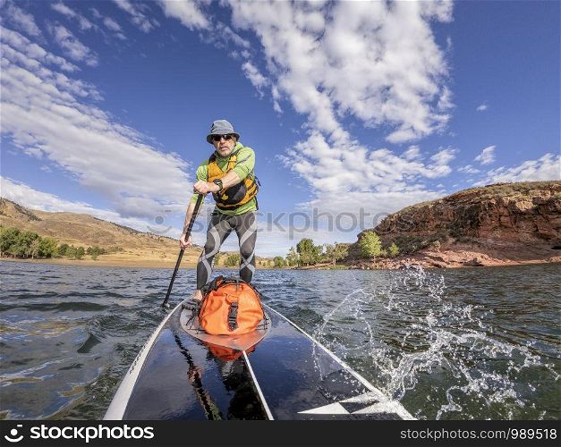 senior man paddling a stand up paddleboard against head wind on mountain lake - Horsetooth Reservoir , Colorado, in early fall scenery