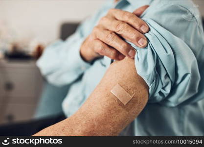 Senior man patient holding shirt sleeve up with a plaster in place of injection of vaccine. Covid-19 or coronavirus vaccination. Man wearing face mask