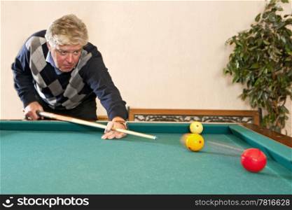 Senior man playing a game of carambole billiards - selective focus on the billiard balls