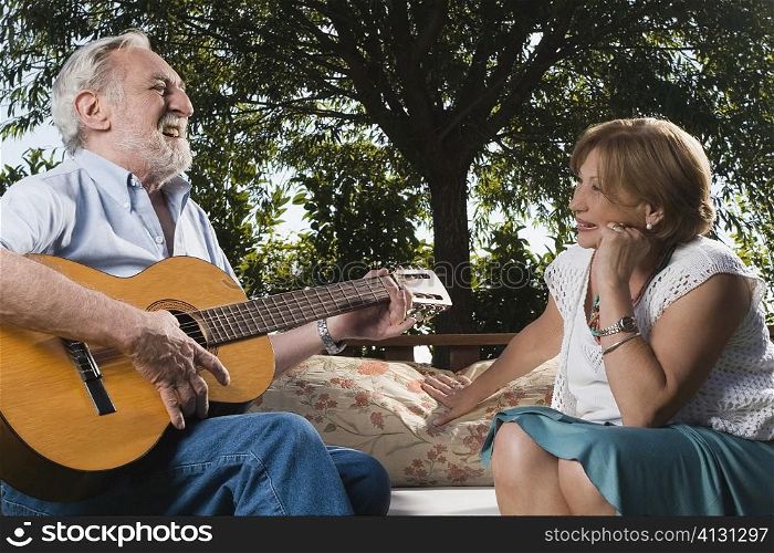 Senior man playing a guitar in front of a senior woman