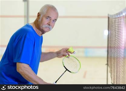 senior man playing badminton on indoor court