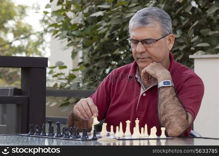 Senior man playing chess game while sitting by table