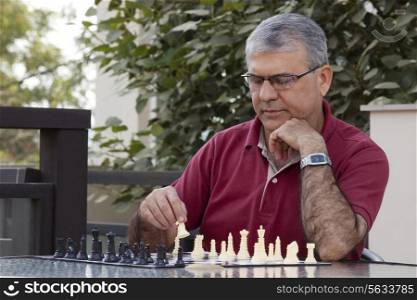 Senior man playing chess game while sitting by table