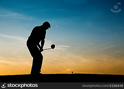 Senior man playing golf - pictured as a silhouette against an evening sky