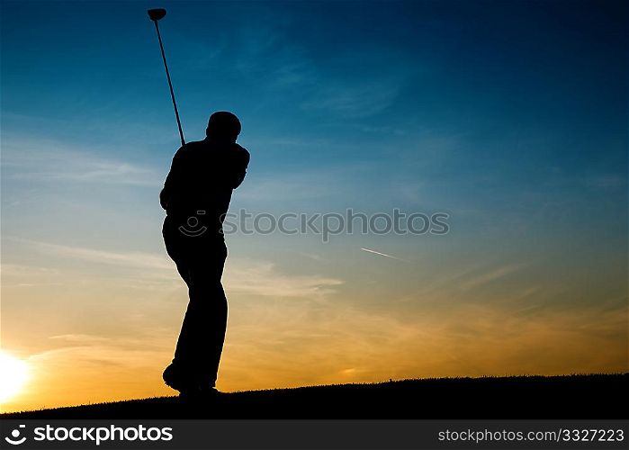 Senior man playing golf - pictured as a silhouette against an evening sky
