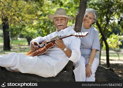 Senior man playing guitar while enjoying at park with mature woman