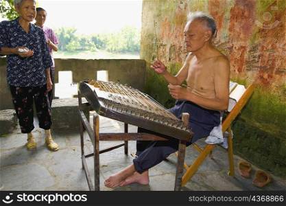 Senior man playing hammered dulcimer with his family standing beside him, Fuli Village, Yangshuo, Guangxi Province, China