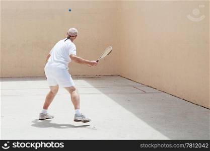 Senior man playing racquetball on an outdoor court.