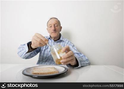 Senior man preparing slice of bread and marmalade at table