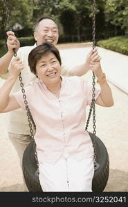 Senior man pushing a mature woman on a swing