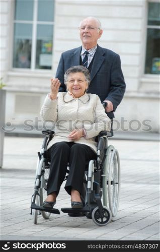 senior man pushing woman in wheelchair in the city
