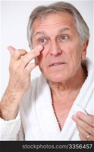 Senior man putting concealer around his eyes