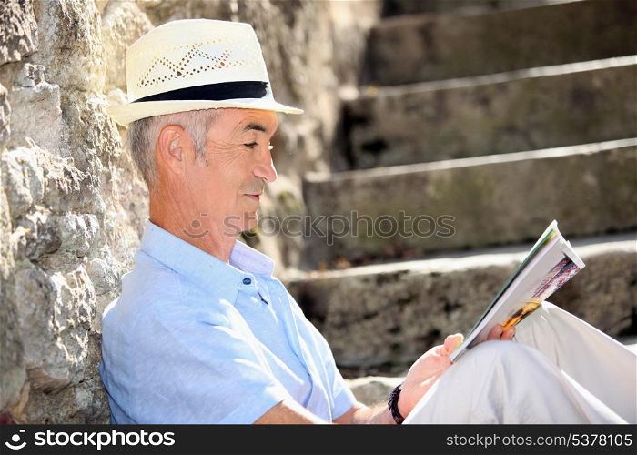 Senior man reading a magazine on some old stone steps