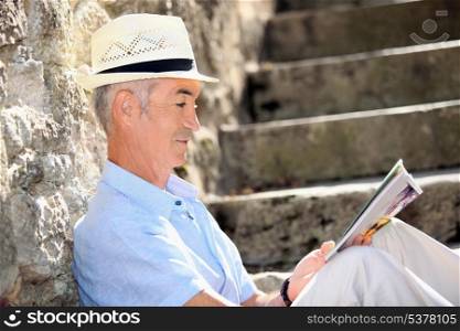 Senior man reading a magazine on some old stone steps