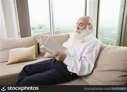 Senior man reading book on sofa in house