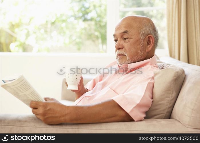 Senior Man Reading Book With Drink At Home