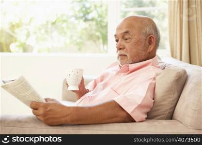 Senior Man Reading Book With Drink At Home