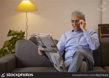 Senior man reading newspaper while sitting on sofa at home 