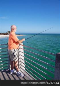 Senior man relaxing and fishing off a pier near the beach.