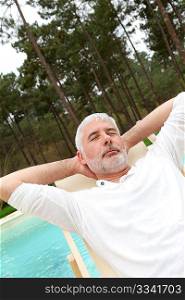 Senior man relaxing in deck chair by a pool