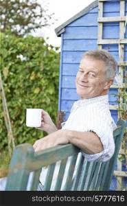 Senior Man Relaxing In Garden With Cup Of Coffee