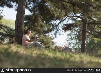 Senior man relaxing under a tree and reading a book in a park in the springtime, Beijing