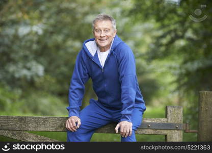 Senior Man Resting On Gate During Exercise In Countryside