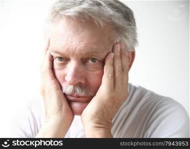 Senior man rests his face in his hands and looks disappointed or bored.