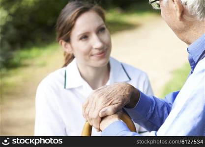 Senior Man&rsquo;s Hands Resting On Walking Stick With Care Worker In Background