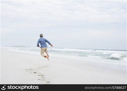 Senior man running and jumping on beach