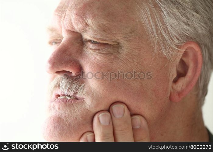 Senior man shows area of pain on his jaw with his fingers.