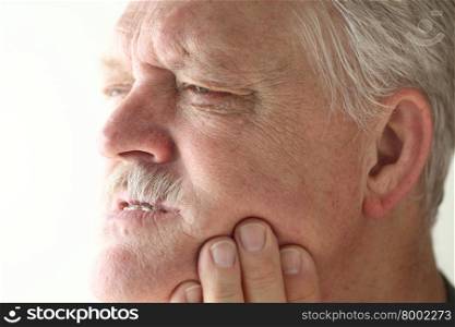 Senior man shows area of pain on his jaw with his fingers.