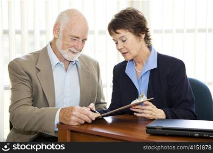 Senior man signing a contract in his attorney&rsquo;s office.
