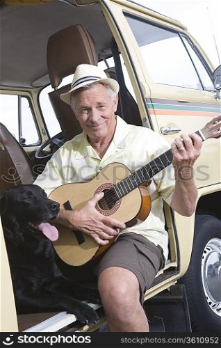 Senior man sits in his campervan with a guitar and his pet dog