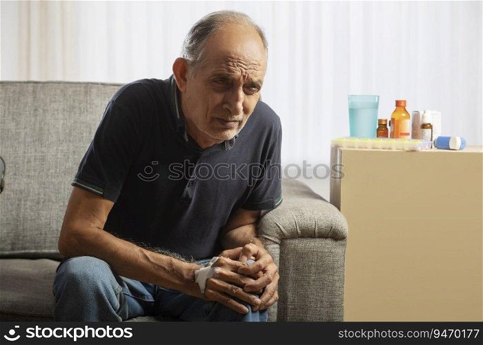 Senior man sitting at home having a knee pain. (Health and fitness)  