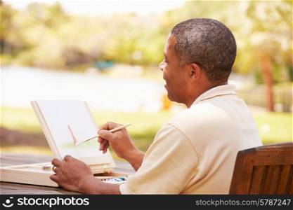 Senior Man Sitting At Outdoor Table Painting Landscape