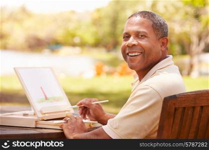 Senior Man Sitting At Outdoor Table Painting Landscape