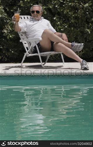 Senior man sitting at the poolside and holding a glass of juice
