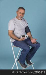 senior man sitting chair checking blood pressure electric tonometer