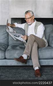 senior man sitting cozy sofa with crossed leg reading newspaper